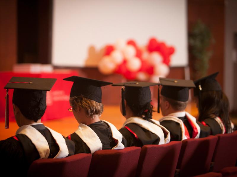 Five students seen from behind in their graduation gowns.